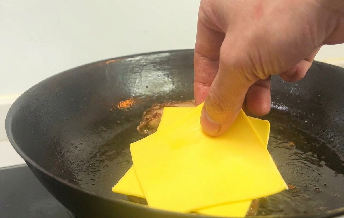 팬 안의 고기 패티 위에 노란 치즈 두 장을 올리는 모습