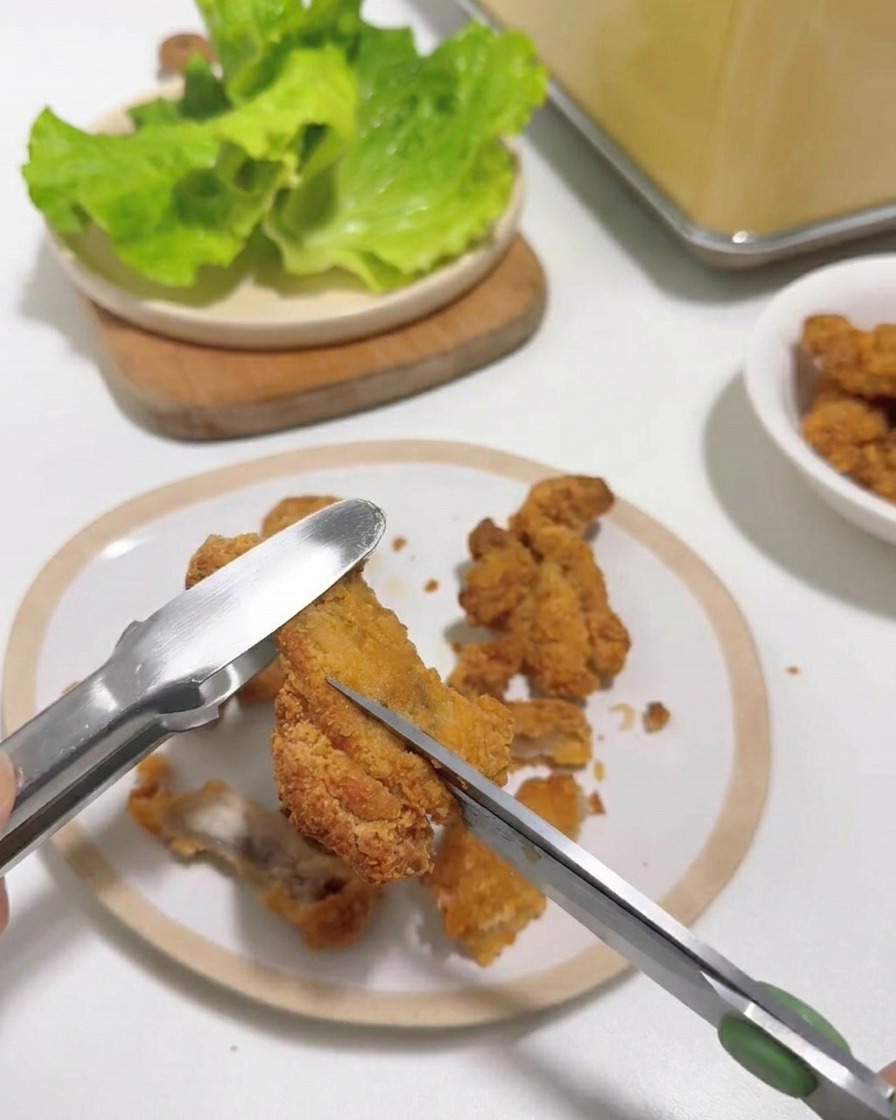 집게로 잡은 뜨거운 치킨을 주방 가위로 일정하게 자르는 모습.