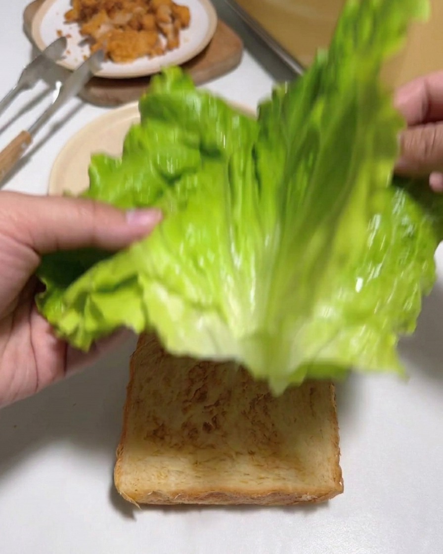 구운 식빵 위에 신선한 상추 잎을 올리는 손길.