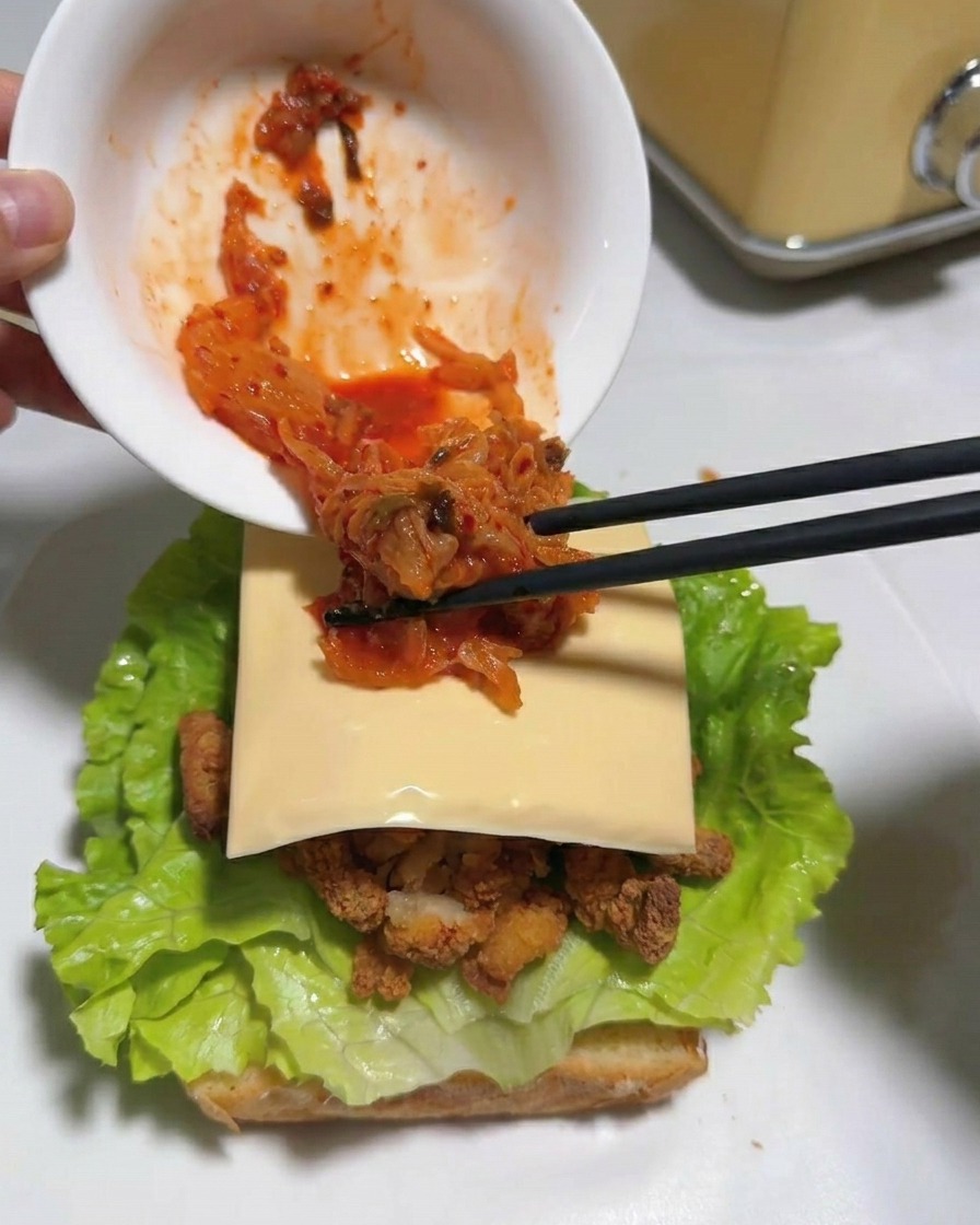 젓가락으로 치즈 위에 다진 빨간 김치를 얹는 모습.