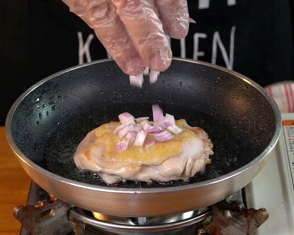 팬 안의 치킨 옆에 다진 적양파와 마늘을 뿌려 넣는 모습