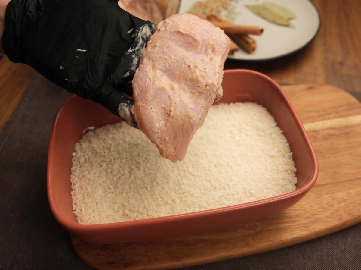 요거트 마리네이드된 치킨을 빵가루가 담긴 쟁반 위에 올려 누르는 모습.