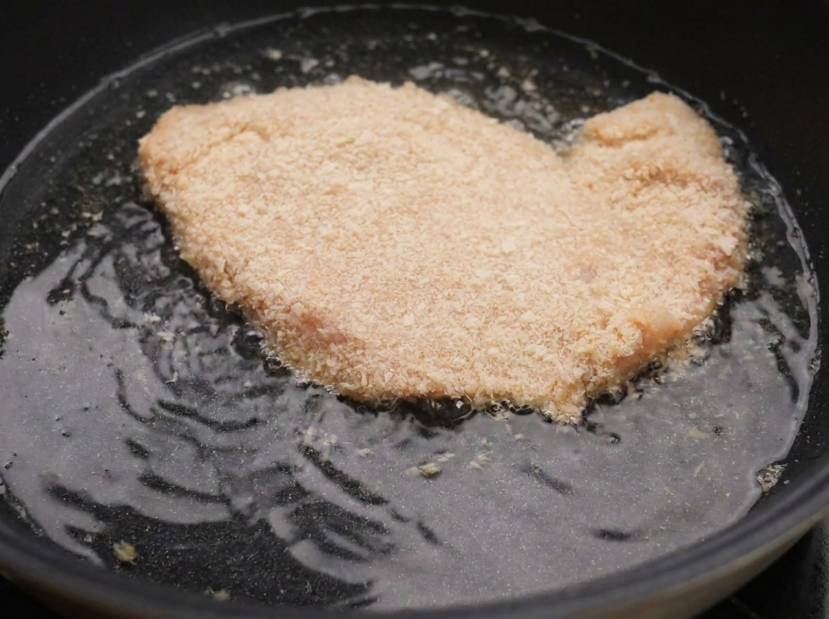 뜨거운 기름이 담긴 팬에서 빵가루 입힌 치킨이 튀겨지는 모습.