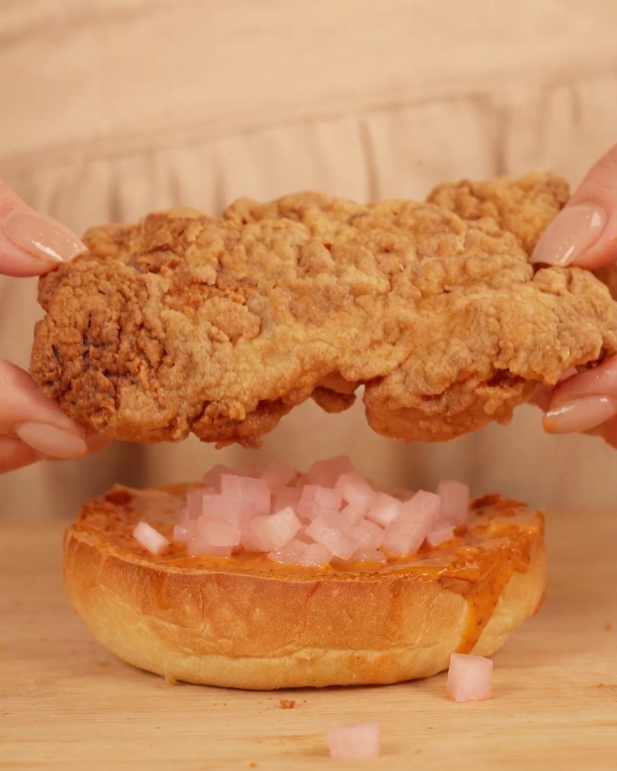 치킨무가 올라간 번 위에 큼직한 프라이드 치킨 패티를 올리는 모습.