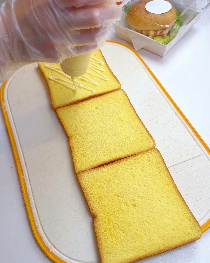 도마 위에 놓인 식빵 세 장 위에 마요네즈를 지그재그로 뿌리는 모습.