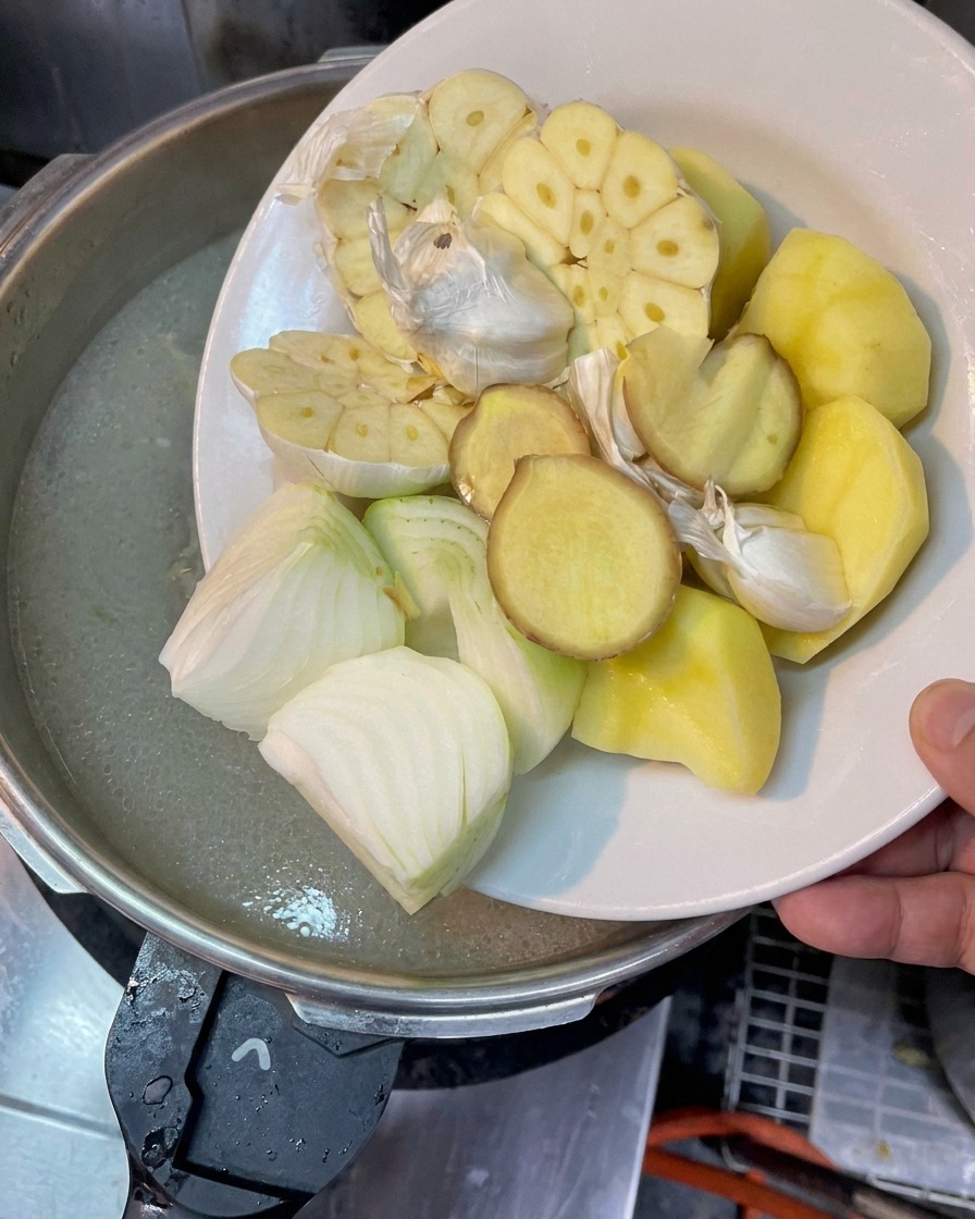 끓는 육수에 반으로 자른 마늘, 양파, 생강 슬라이스, 감자를 넣는 모습