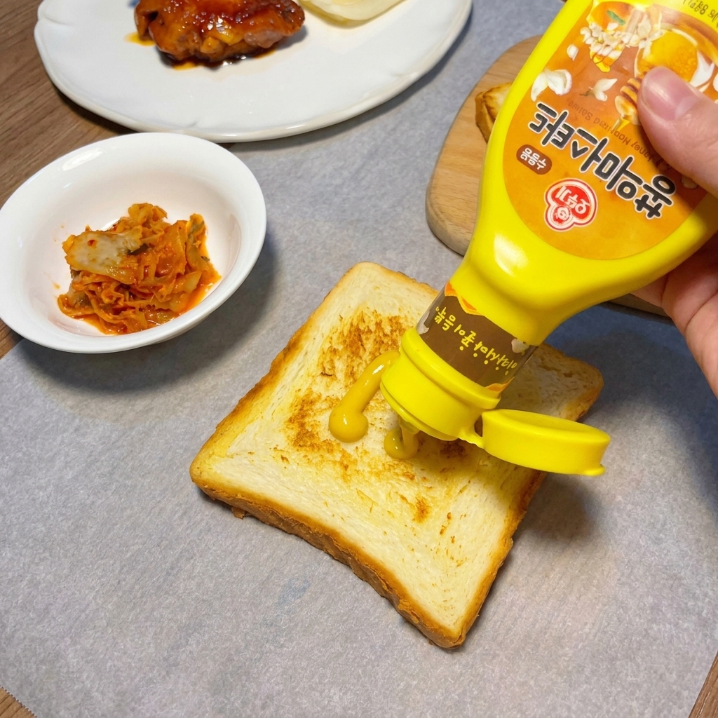 구운 식빵 위에 노란 머스터드 소스를 지그재그로 뿌리는 모습.