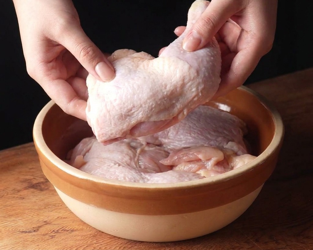 나무 도마 위 베이지색 세라믹 볼에 생 닭다리살을 담고 있는 모습.