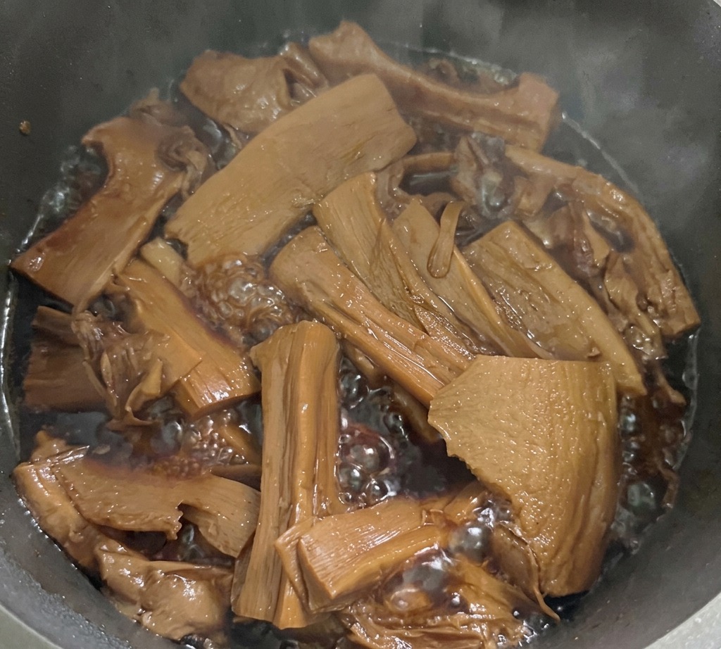 가스레인지 위에 놓인 냄비에서 얇게 썬 죽순이 진한 갈색 양념에 졸여지고 있는 모습.