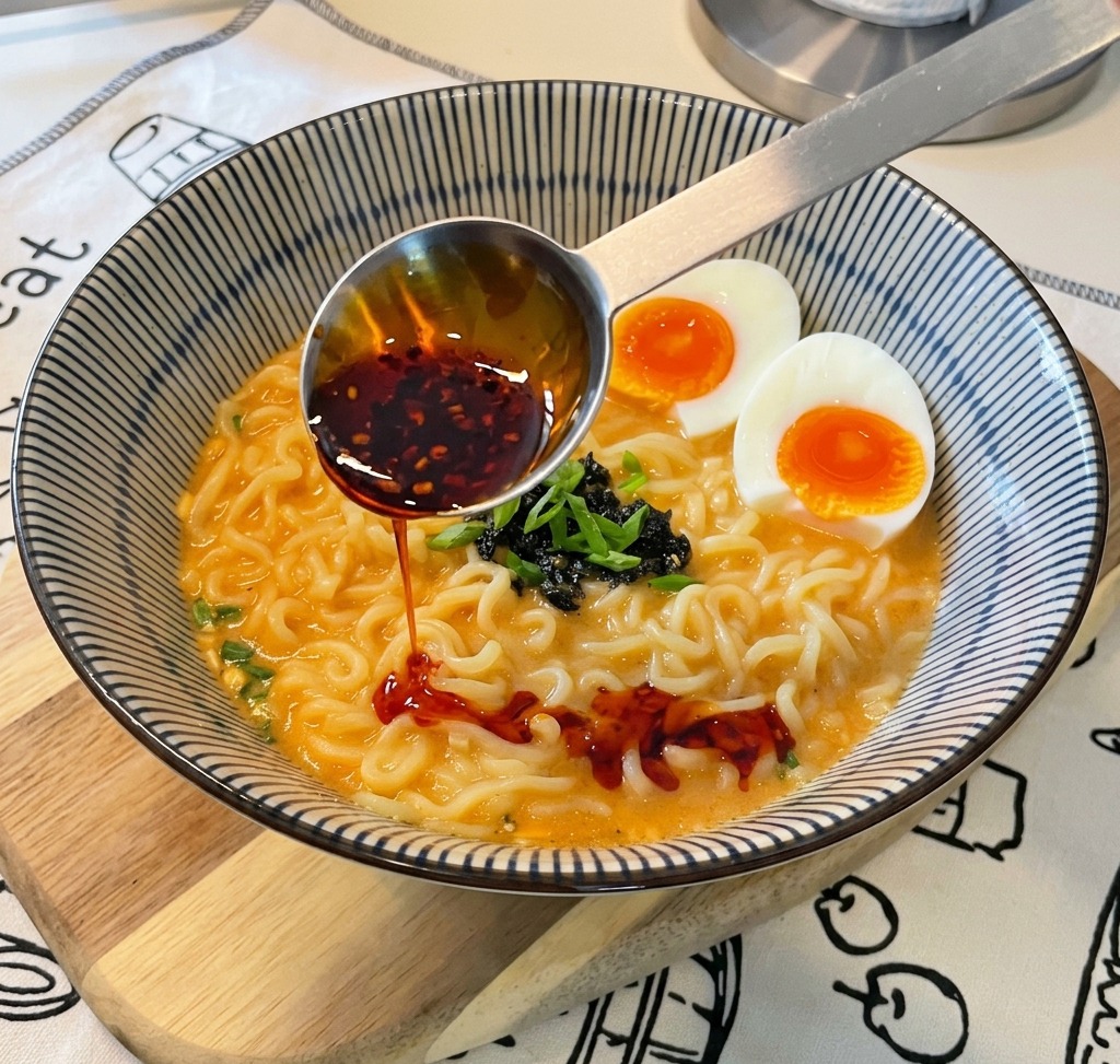 완성된 라면 그릇에 계량스푼으로 고추기름을 떨어뜨려 붉은 마블링을 만드는 모습.