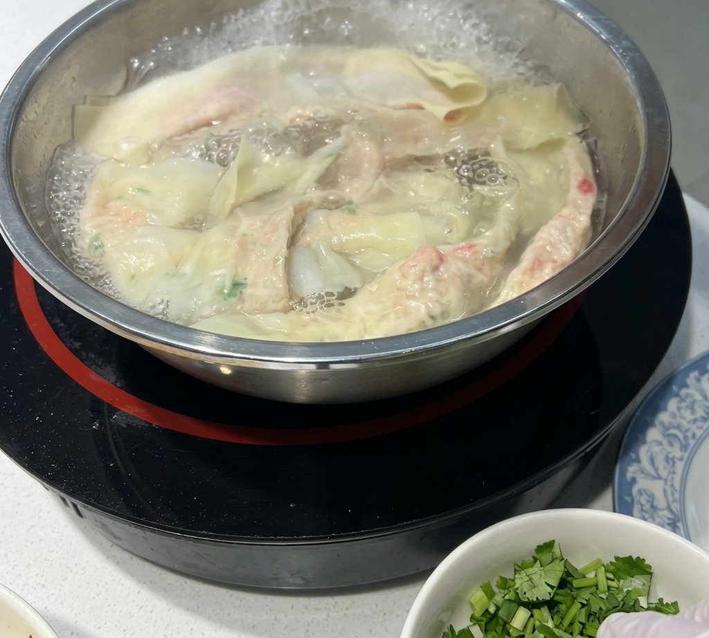 스테인리스 냄비의 끓는 물 속에서 수제 완탕면이 익어가고 있으며 일부 면이 표면으로 떠오른 모습.