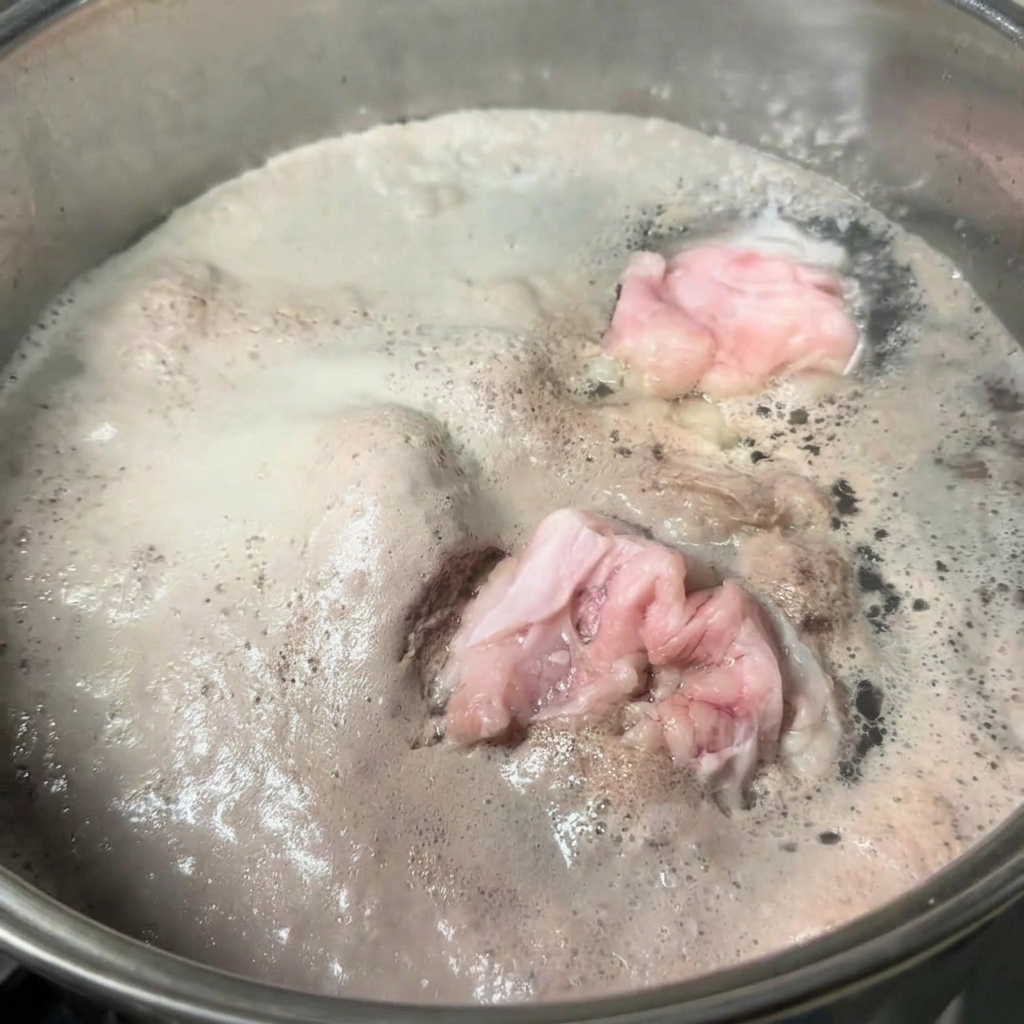 팔팔 끓는 물 속의 돼지 뼈 위로 회색빛 거품이 두껍게 떠오른 스테인리스 냄비.