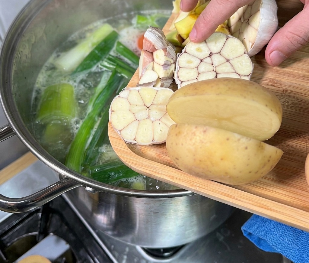 도마 위에 반으로 자른 통마늘과 감자를 김이 모락모락 나는 사골 육수 냄비에 넣는 손길.