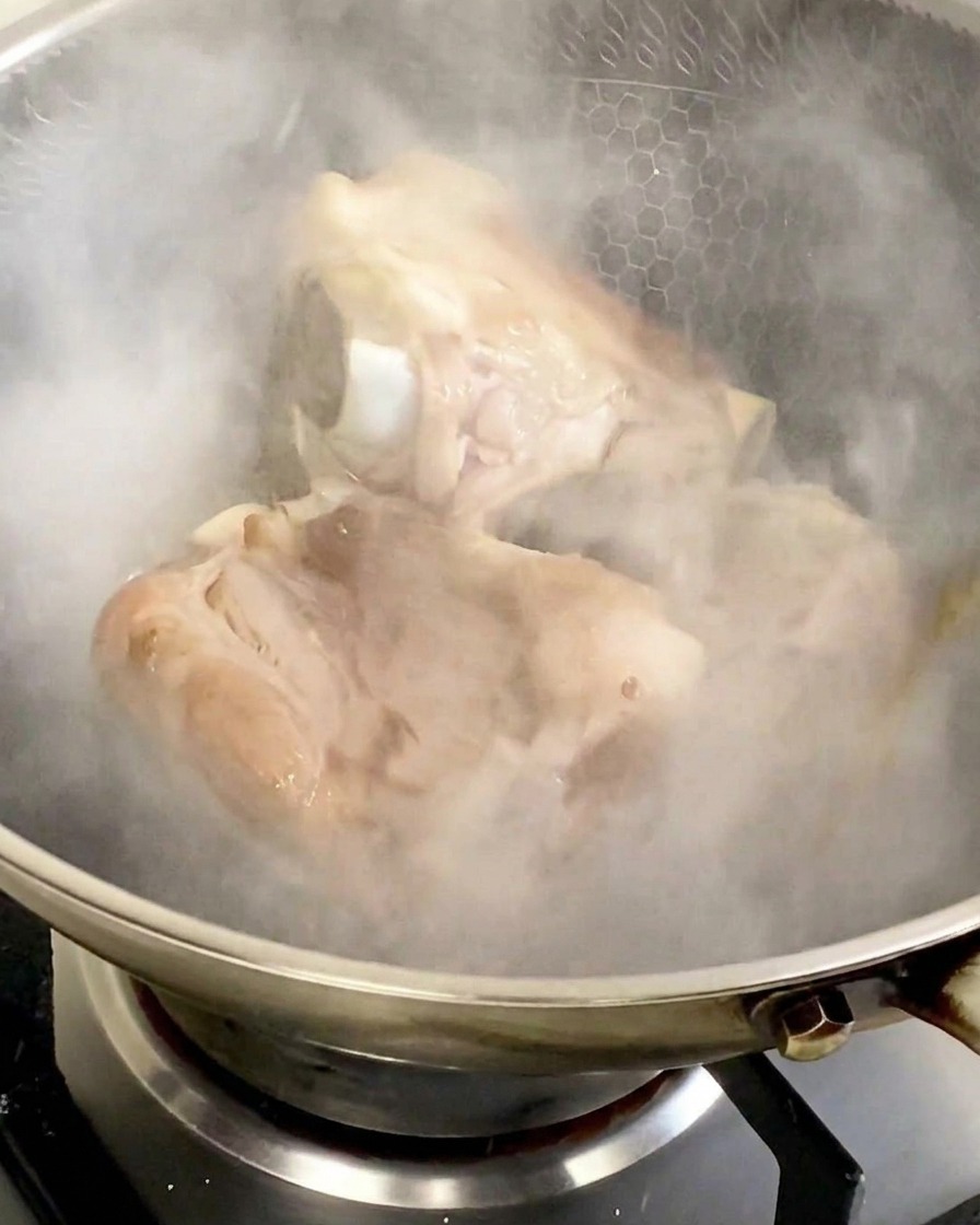 스테인리스 웍에 맛술을 부어 하얀 증기가 확 피어오르는 가운데 돼지 등뼈가 갇혀 있는 모습.