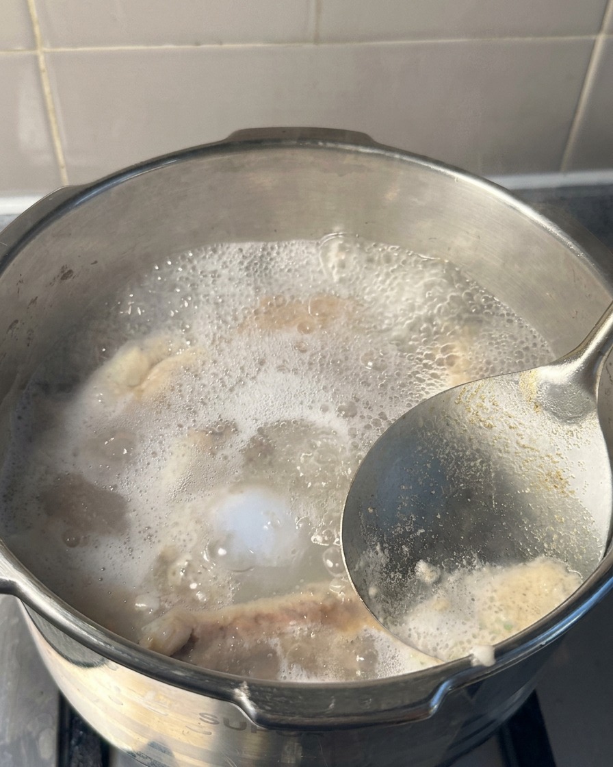 압력솥 안의 끓는 물 표면에서 메탈 국자로 하얗고 회색빛이 도는 거품을 떠내고 있는 접사 사진