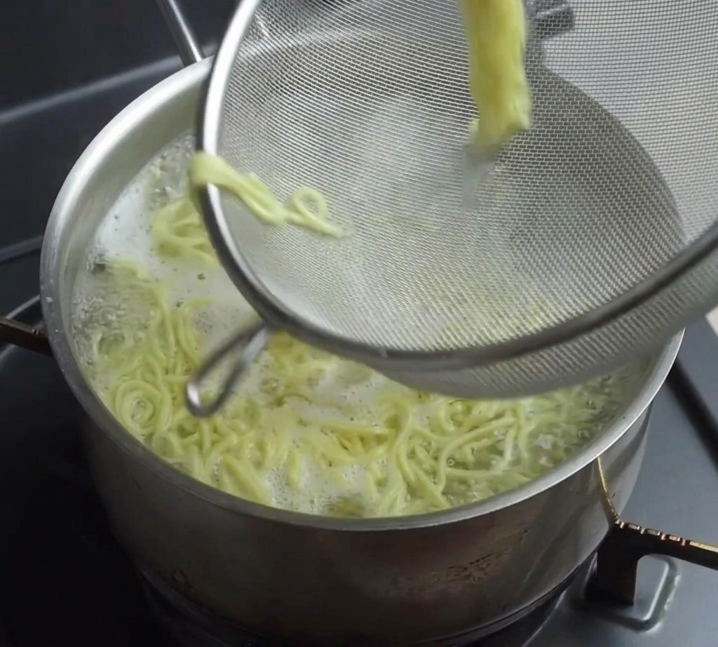 김이 나는 냄비에서 건져 올린 노란 라멘 면발이 담긴 채반의 모습.