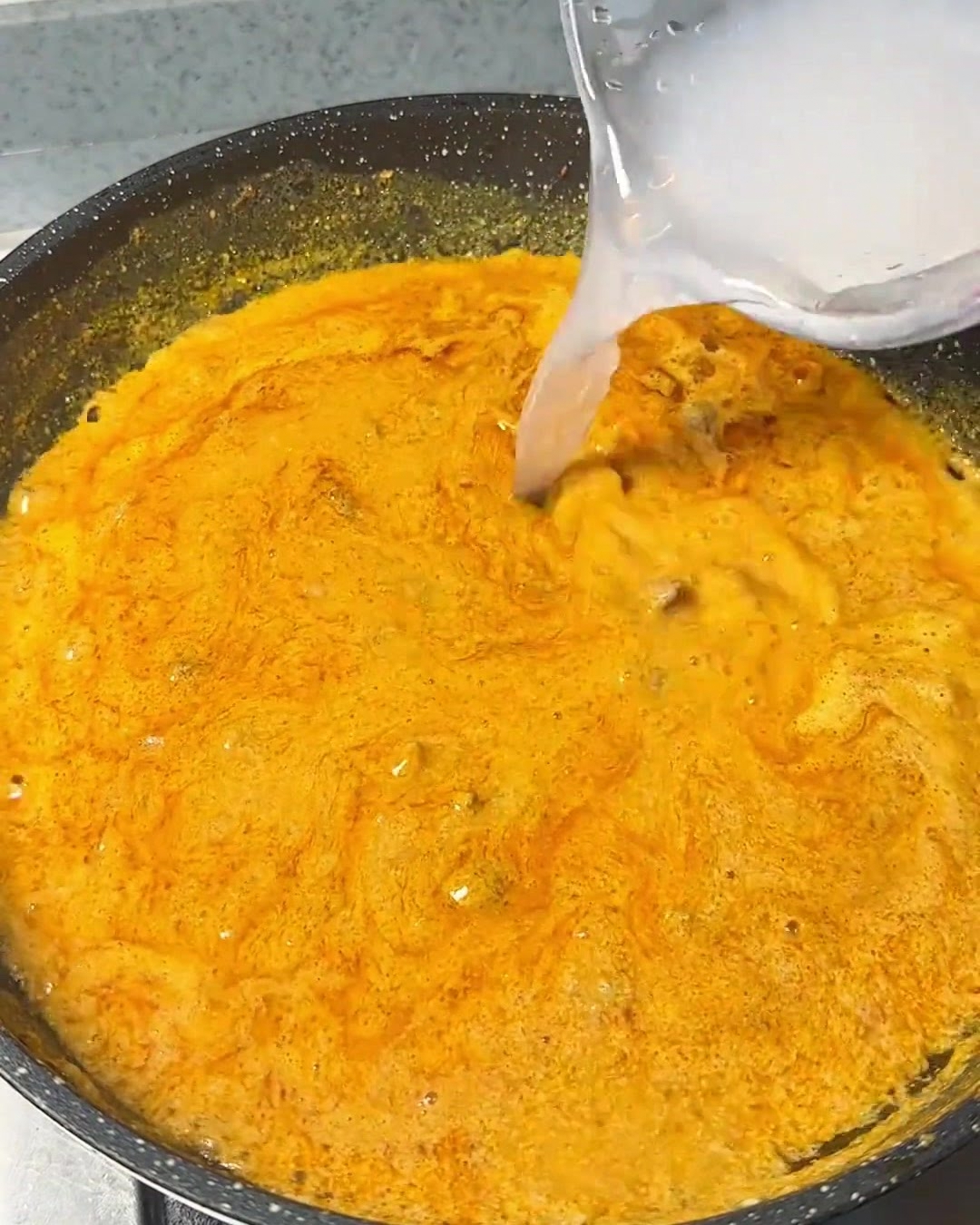 팬에서 보글보글 끓어오르는 진한 오렌지빛 카레 소스에 투명한 물을 부어주는 모습