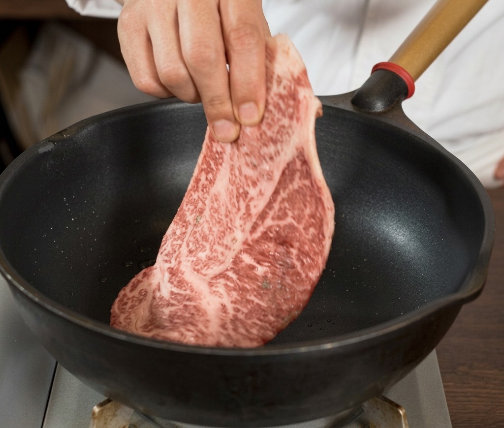 달구어진 검은색 팬에 후추로 밑간을 한 두툼하고 마블링이 좋은 생스테이크를 올리는 손