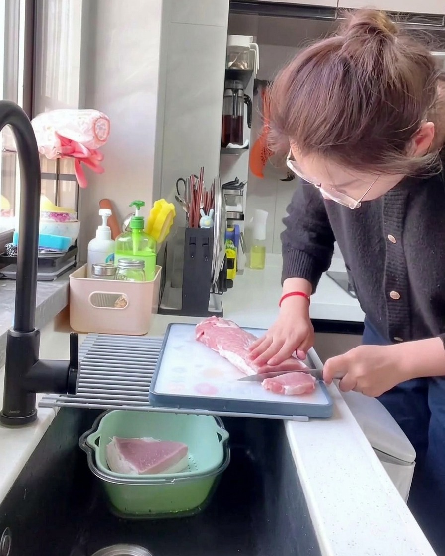 하얀 도마 위에서 주방용 칼로 생 돼지고기 등심을 1cm 두께로 일정하게 썰고 있는 모습.