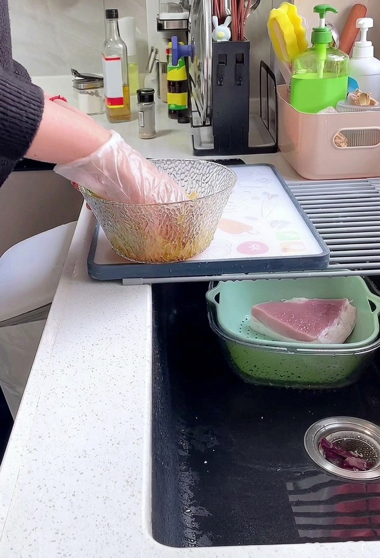 유리 볼 안에서 간장, 후추, 전분 양념에 도톰한 돼지고기 등심을 비닐장갑을 낀 손으로 골고루 버무리는 모습.