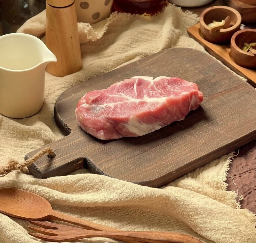 도마 위에 올려진 생 돼지 목살과 주변의 조리 도구들.