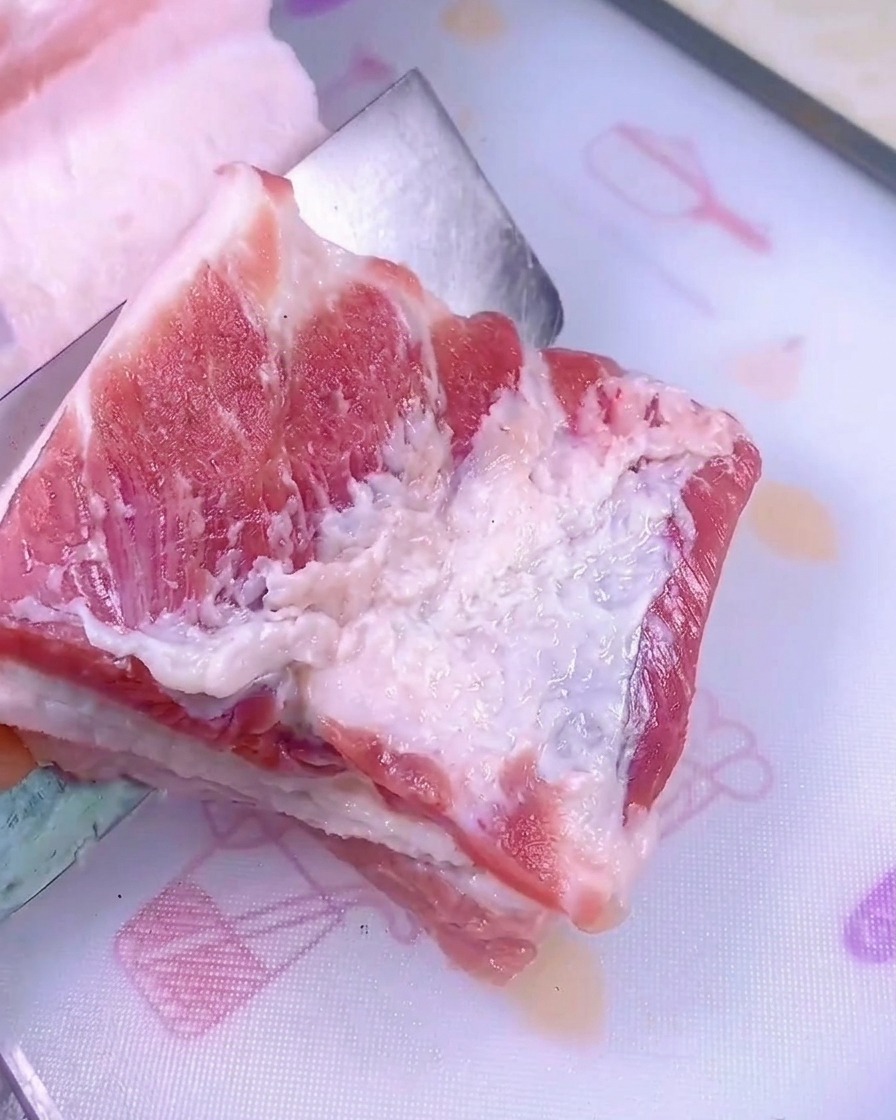 하얀색 플라스틱 도마 위에서 잘 드는 칼로 두툼한 생삼겹살 덩어리를 썰고 있는 모습.