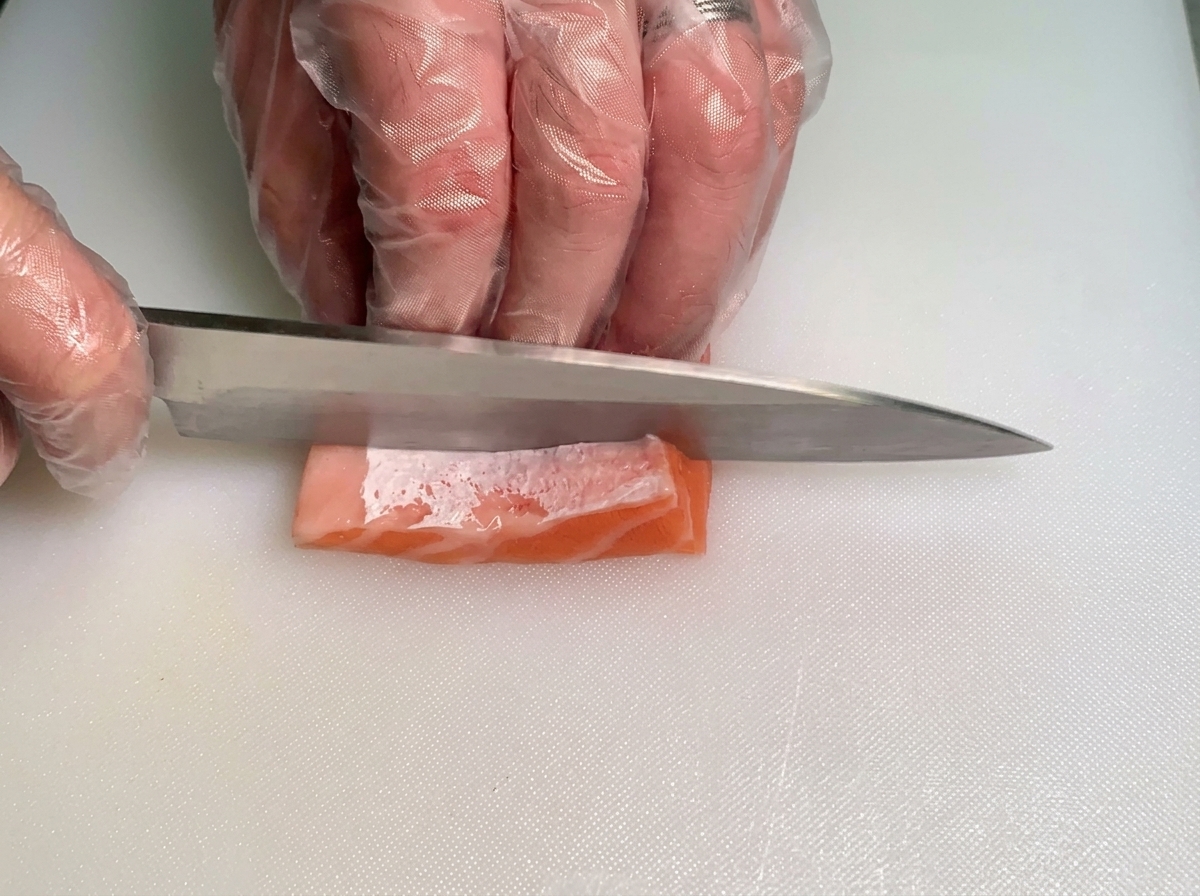 흰색 도마 위에서 칼을 사용해 지방이 풍부한 생연어 뱃살 조각을 얇은 스트립 형태로 조심스럽게 써는 셰프의 모습