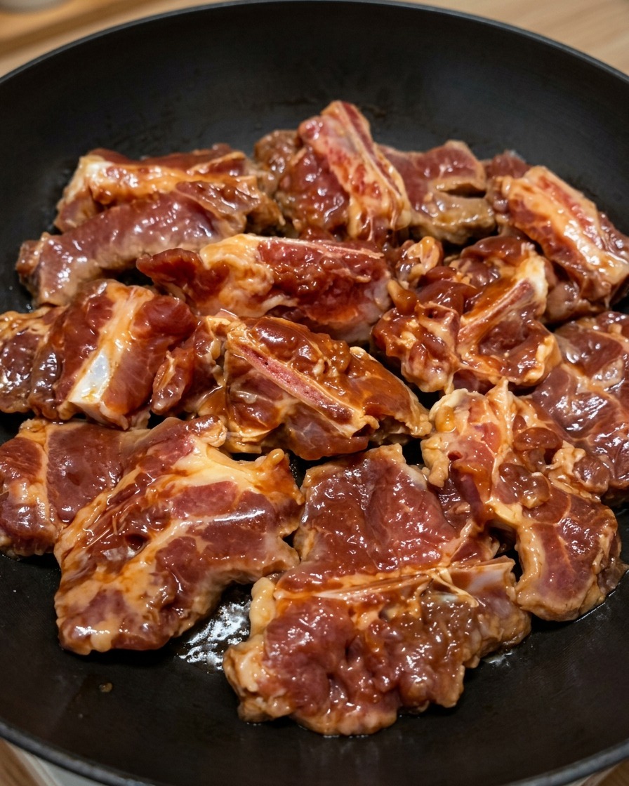 납작하고 검은 프라이팬 위에 겹치지 않게 한 겹으로 가지런히 올려진 양념된 돼지갈비.
