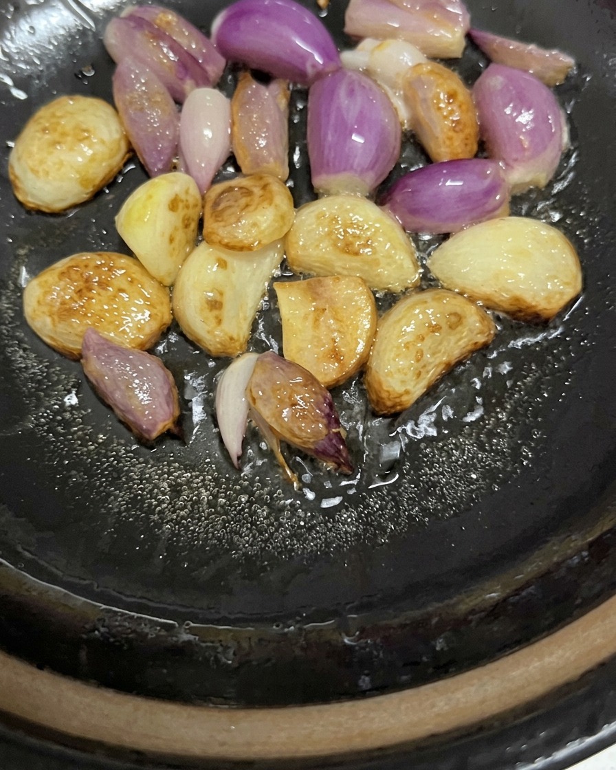 팬 바닥의 기름에서 지글지글 소리를 내며 노릇하게 익어가는 통마늘과 자줏빛 샬롯.