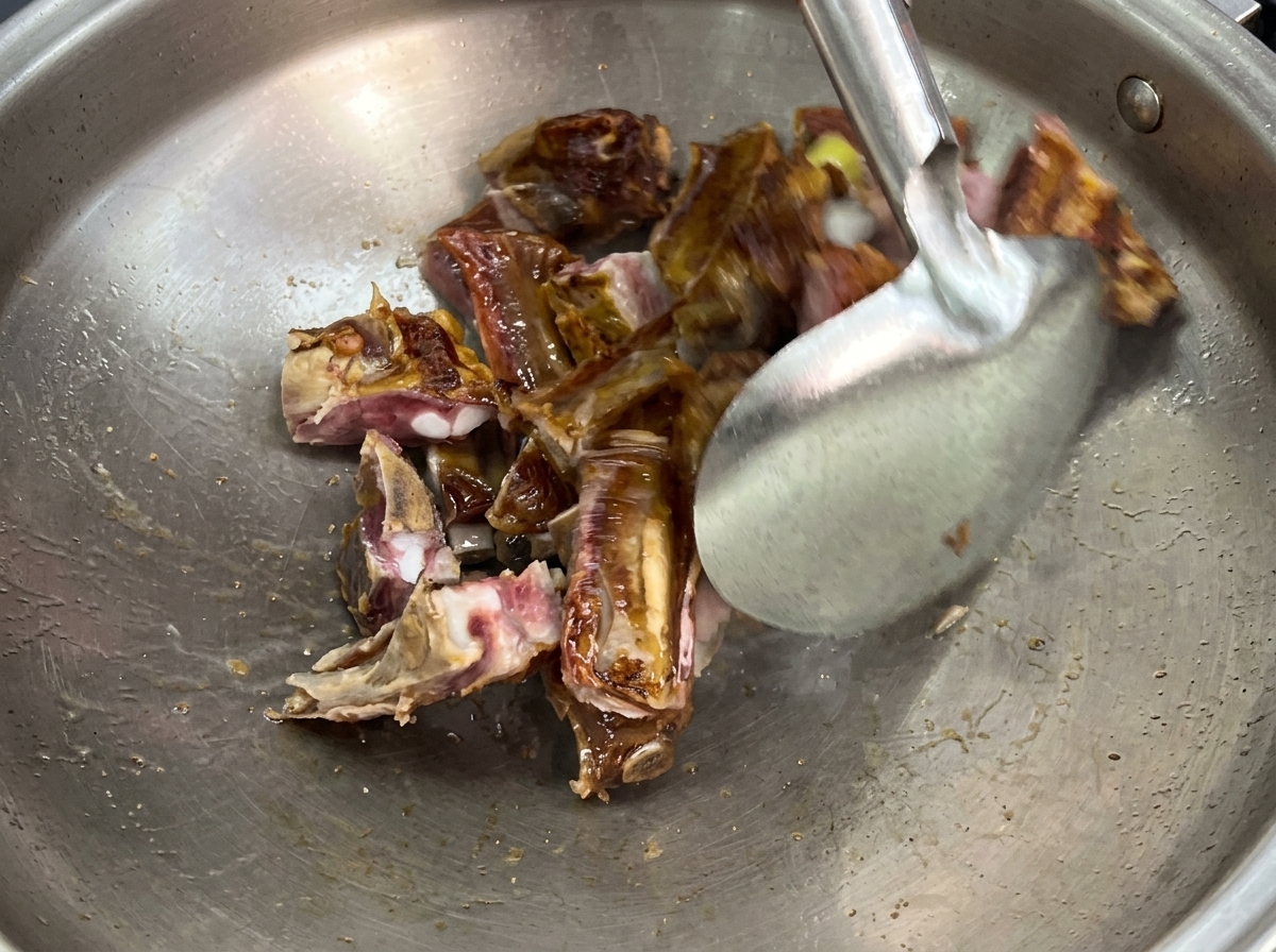 커다란 스테인리스 웍 안에서 쇠뒤집개로 훈제 등갈비 조각과 편 썬 생강을 함께 볶는 모습.