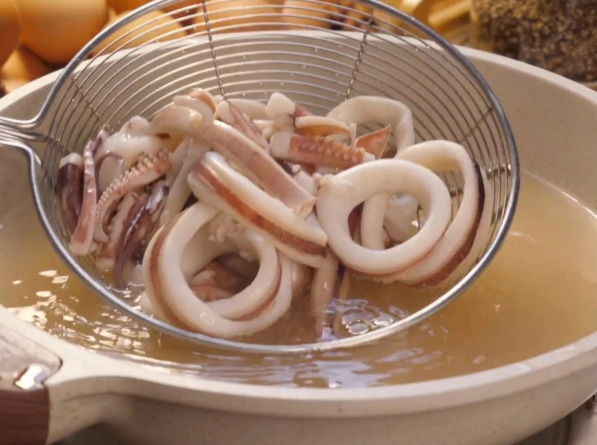 끓는 물이 담긴 냄비에서 건져 올려지는 체에 담긴 오징어 링.