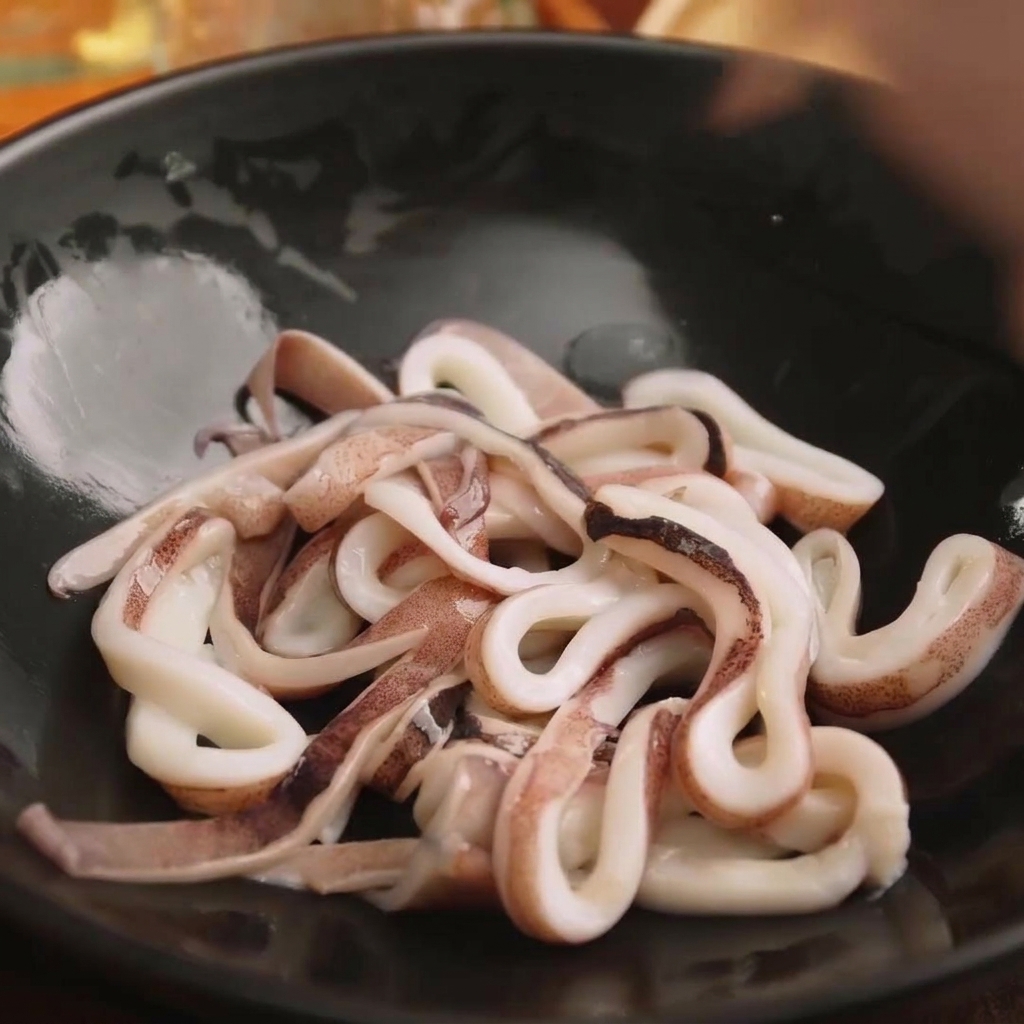 검은색 믹싱 볼에 담겨 양념할 준비가 된 신선한 오징어 링의 모습