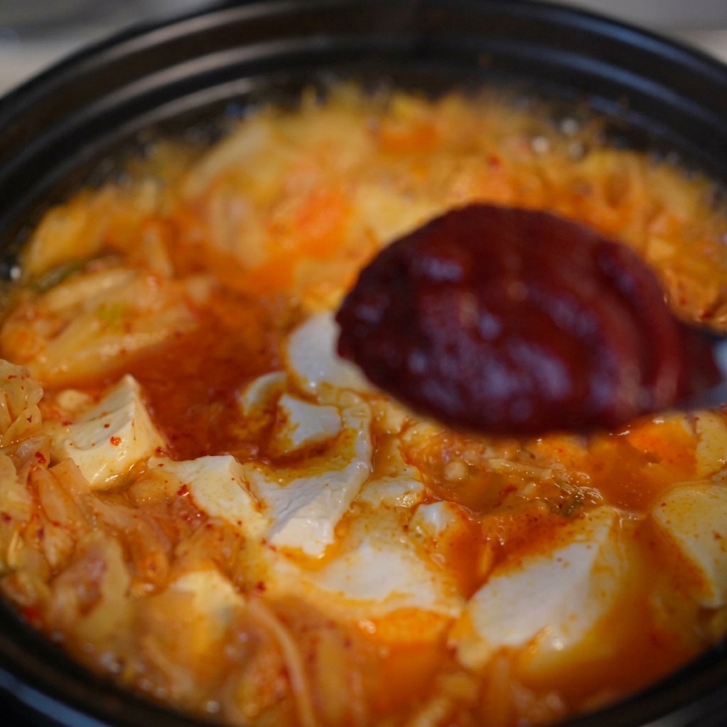 보글보글 끓고 있는 김치 순두부찌개 국물 위로 고추장을 한 숟가락 크게 떠 넣는 모습