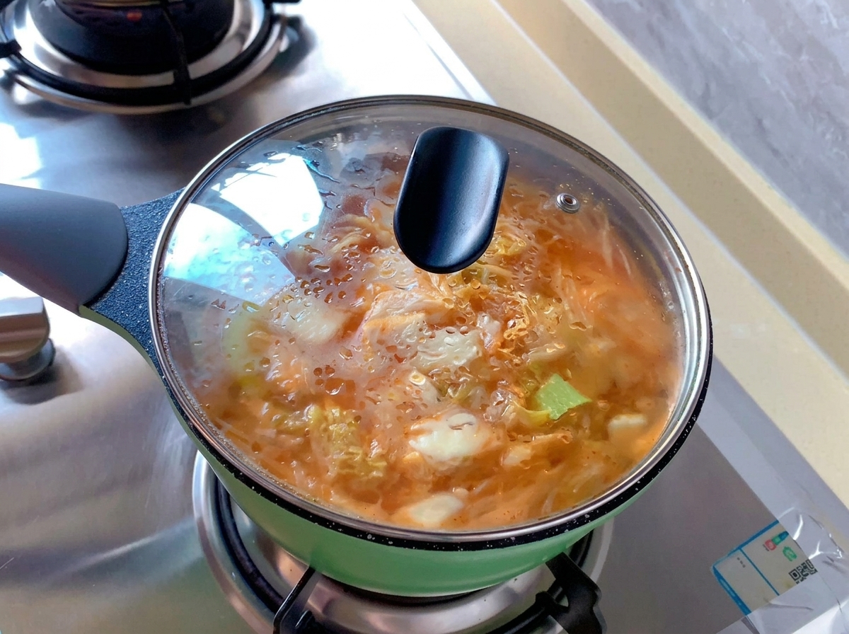 김치찌개가 끓고 있는 초록색 냄비 위에 수증기가 맺힌 투명한 유리 뚜껑이 닫혀 있는 모습