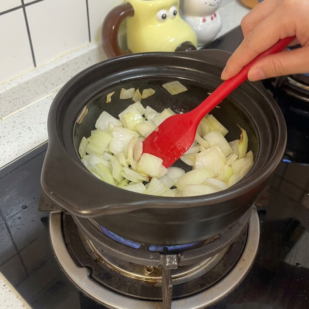 가스레인지 위 뚝배기에서 양파를 붉은색 주걱으로 볶고 있는 모습.