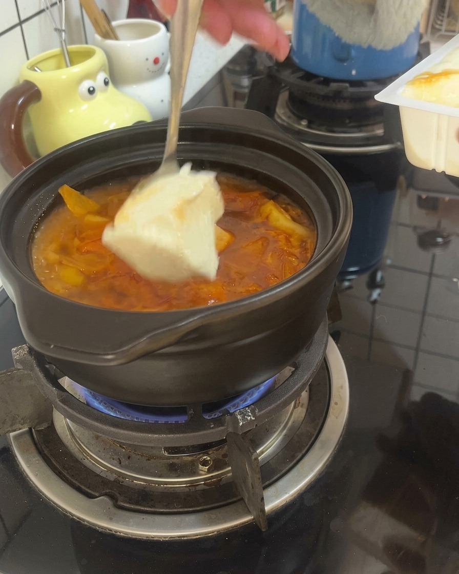 끓고 있는 찌개에 숟가락으로 순두부를 큼직하게 떼어 넣는 모습.
