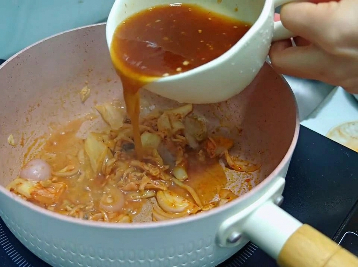 볶은 양파와 김치가 담긴 냄비에 준비해 둔 붉은색 양념장을 붓고 있는 모습
