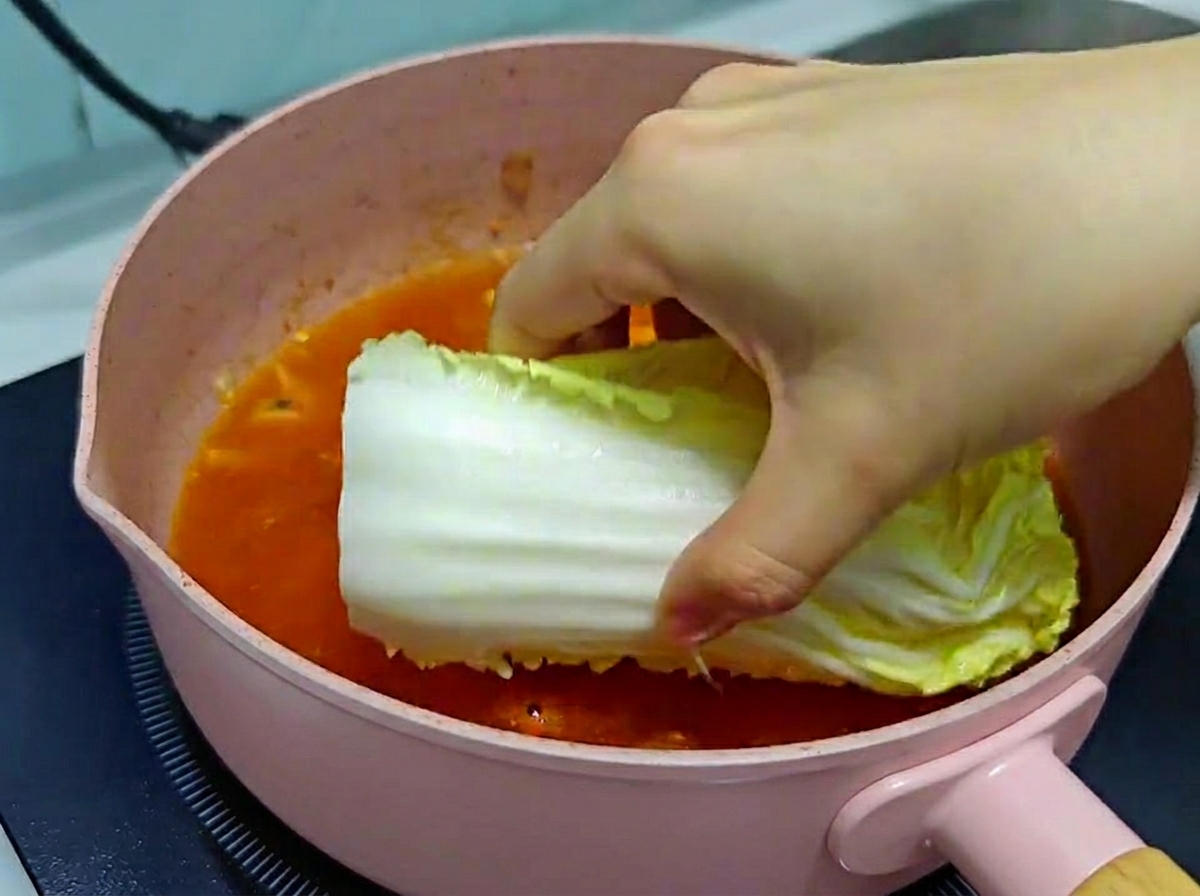 보글보글 끓는 김치찌개 국물에 신선한 배춧잎을 조심스럽게 넣는 손