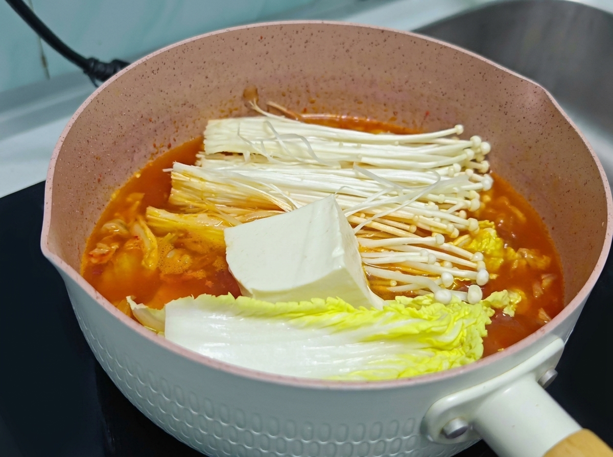 김치찌개 국물 속 배추와 팽이버섯 위에 두툼하게 썬 신선한 흰 두부가 올려져 있는 모습