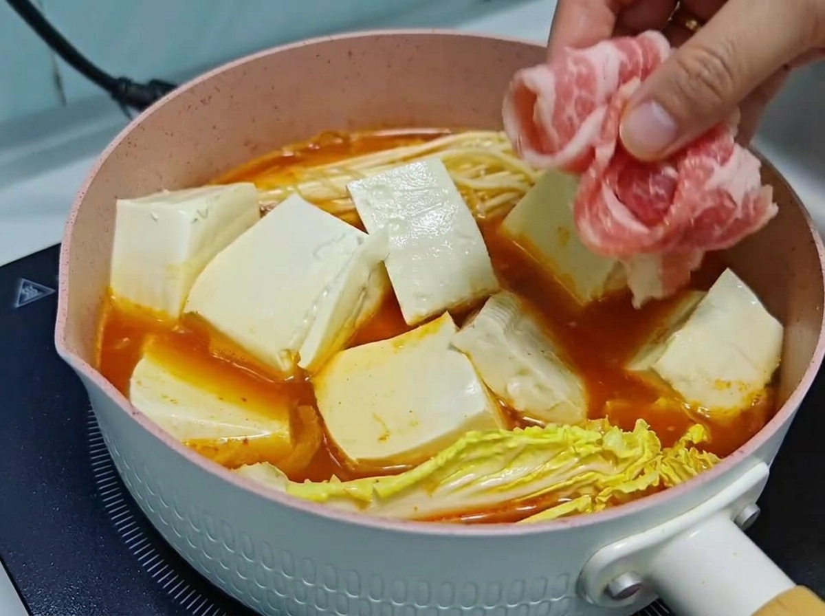 끓고 있는 김치찌개 냄비 속 두부와 야채 위에 얇게 말린 소고기를 차곡차곡 올리는 모습