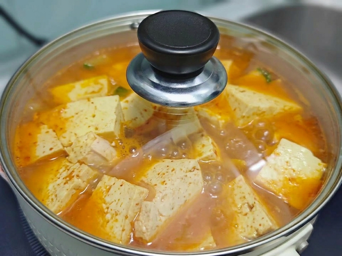 보글보글 끓고 있는 얼큰한 소고기 김치 두부찌개 냄비를 투명한 유리 뚜껑으로 덮어놓은 모습