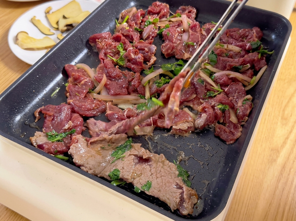 양파, 고수와 함께 버무려진 얇게 썬 양념 소고기를 집게를 이용해 달구어진 전기 불판 위에 올리는 모습