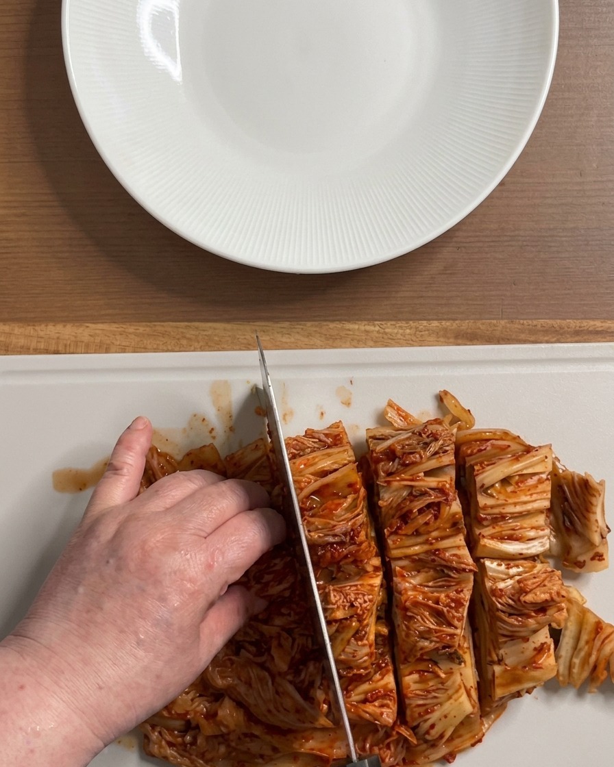 하얀 도마 위에서 붉고 먹음직스러운 신김치 한 포기를 먹기 좋은 크기로 자르는 손