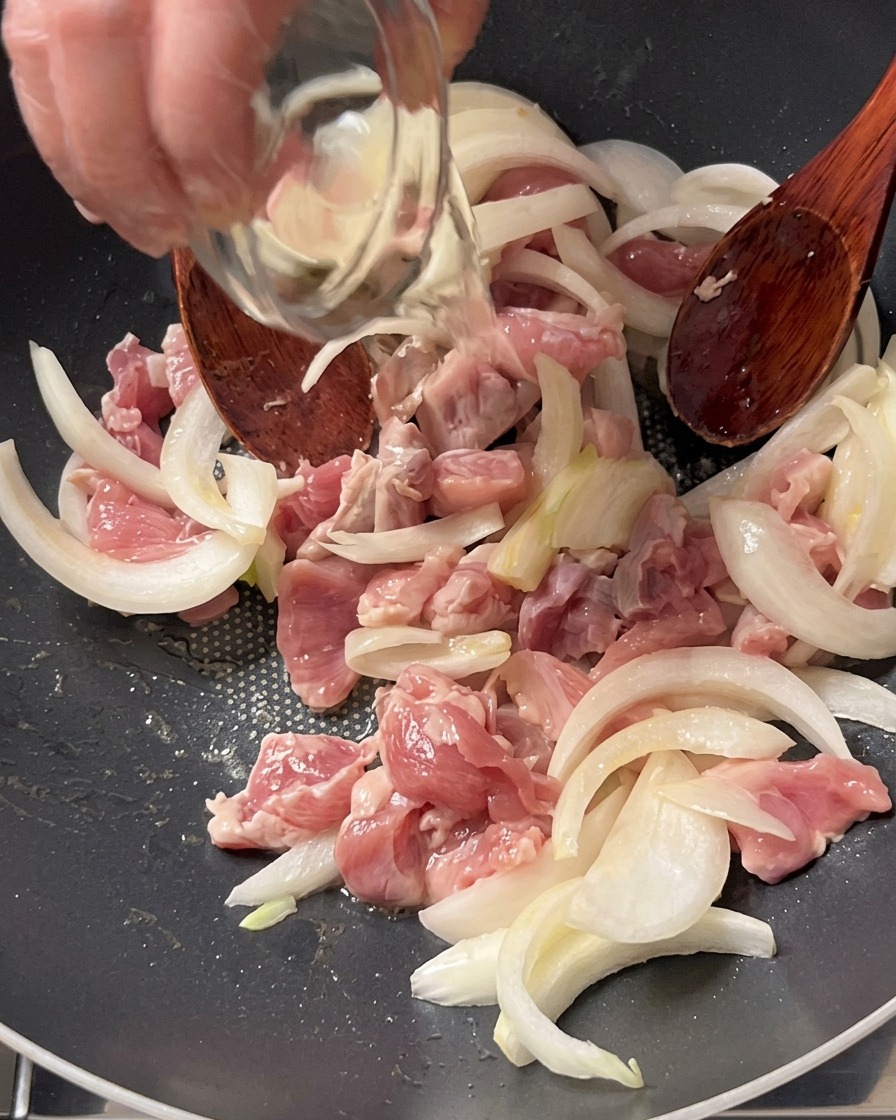 팬 속의 돼지고기와 양파 위로 작은 유리볼에 담긴 맛술을 붓는 모습