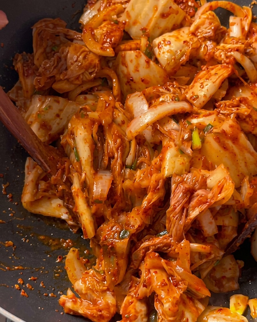 깊은 검은색 웍에서 나무 뒤집개를 사용하여 돼지고기, 양파와 함께 김치를 골고루 볶아내는 모습