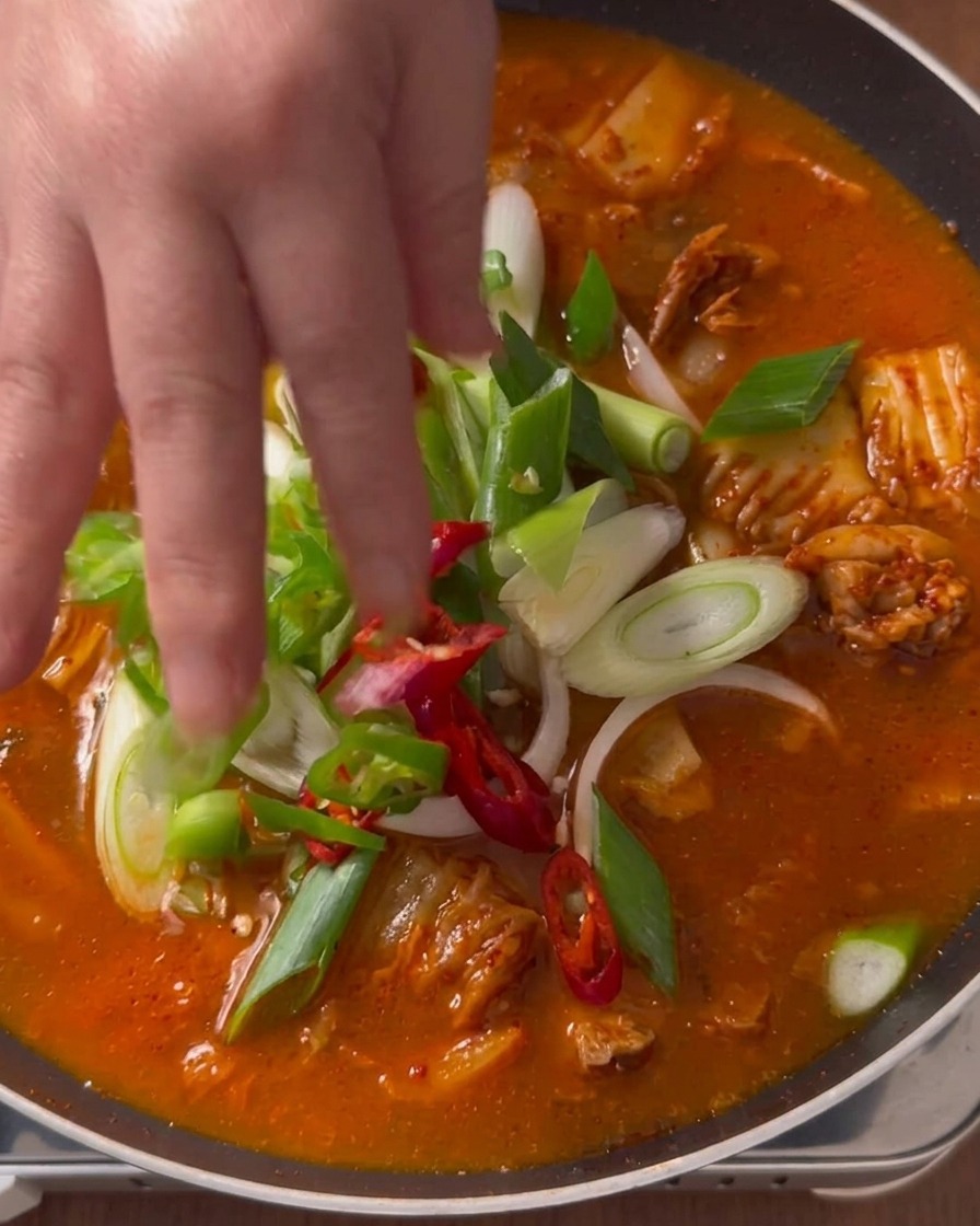 보글보글 끓고 있는 붉은 김치찌개 위에 어슷 썬 대파, 청양고추, 홍고추를 손으로 정성스레 올리는 모습