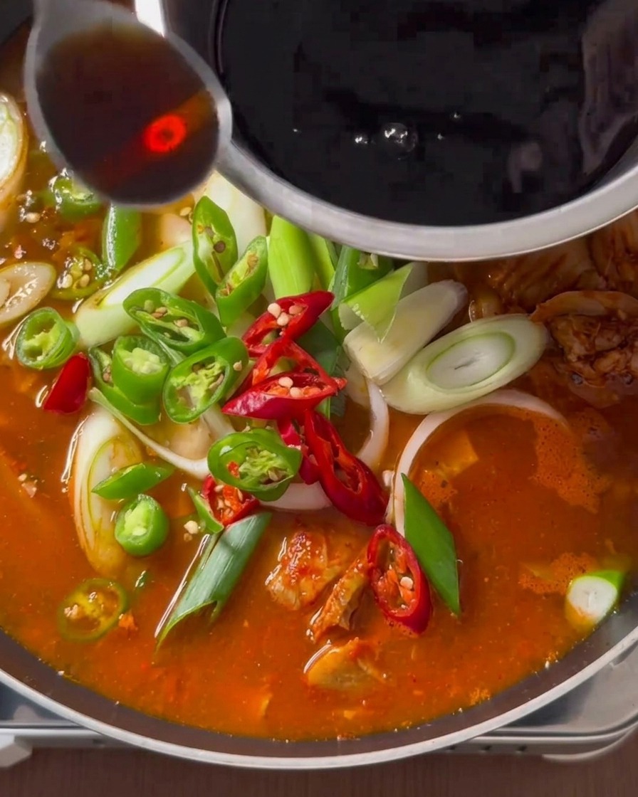 대파와 고추가 올라간 찌개가 끓고 있는 팬 위로 스테인리스 볼에 담긴 진한 액체 양념 한 숟가락을 끼얹는 모습