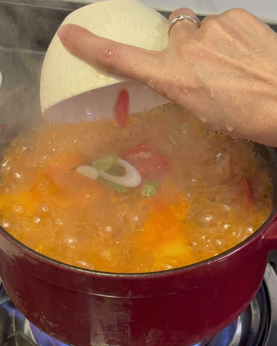 김이 모락모락 나는 보글보글한 김치찌개 위에 흰 접시에서 송송 썬 대파와 고추 고명을 뿌리는 모습.