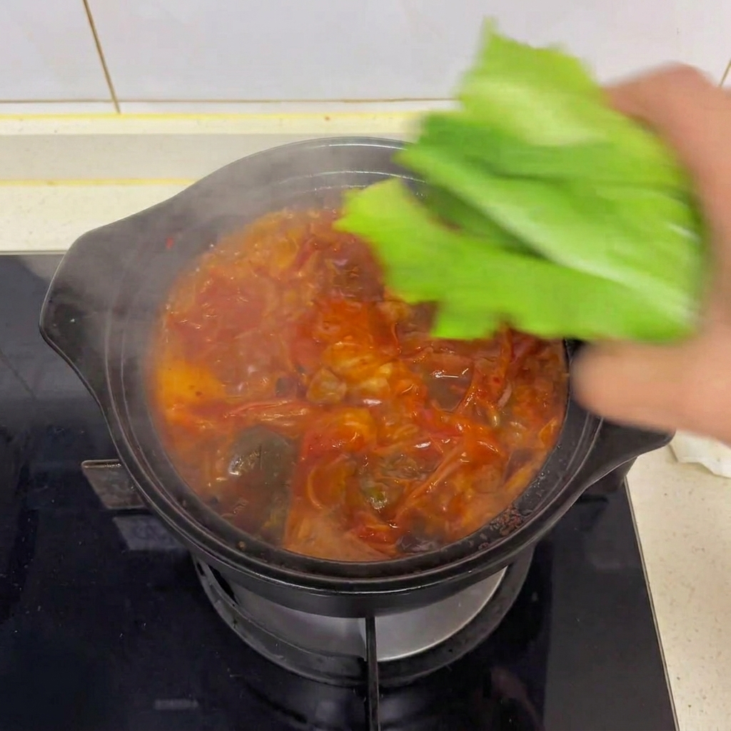 김이 모락모락 나는 뜨거운 김치 두부찌개 위에 신선한 초록색 로메인 상추 잎을 올리는 손.