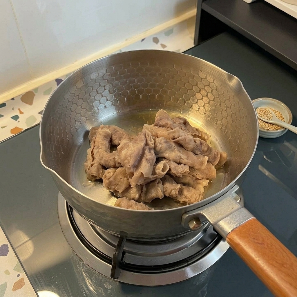 가스레인지 위 엠보싱 패턴이 있는 스테인리스 냄비에서 얇게 썬 소고기를 볶는 모습